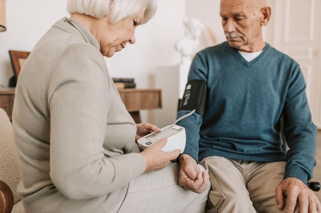 An older woman measures her husband’s blood pressure at home
