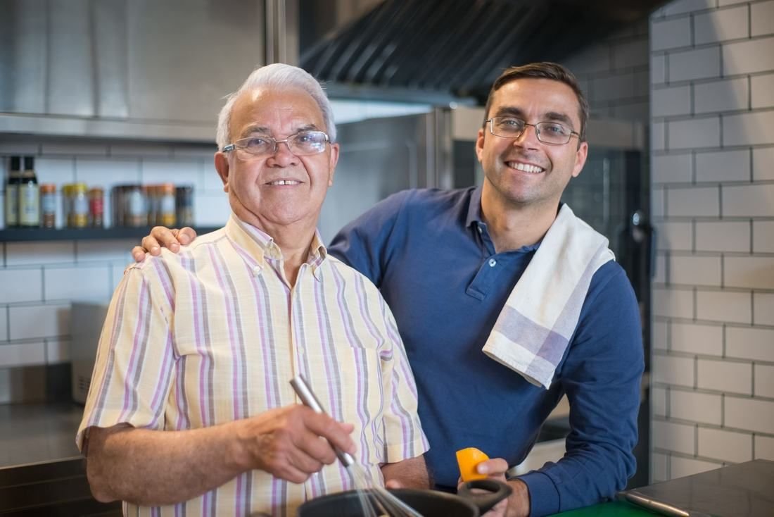An adult son cooking with his father